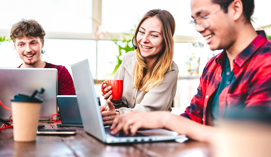 Three young people sitting at table with laptops. 