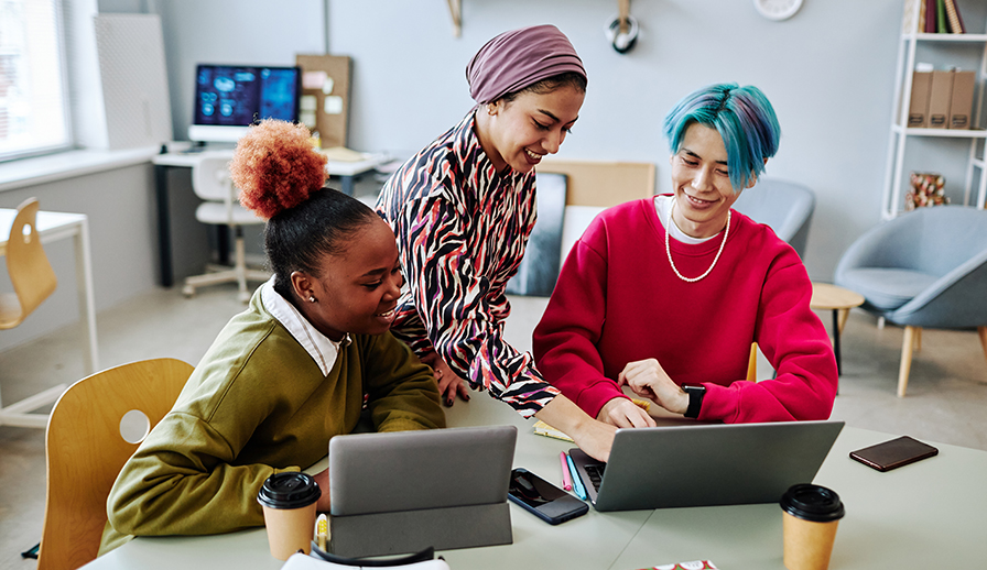 Three young people sitting at table with laptops. 