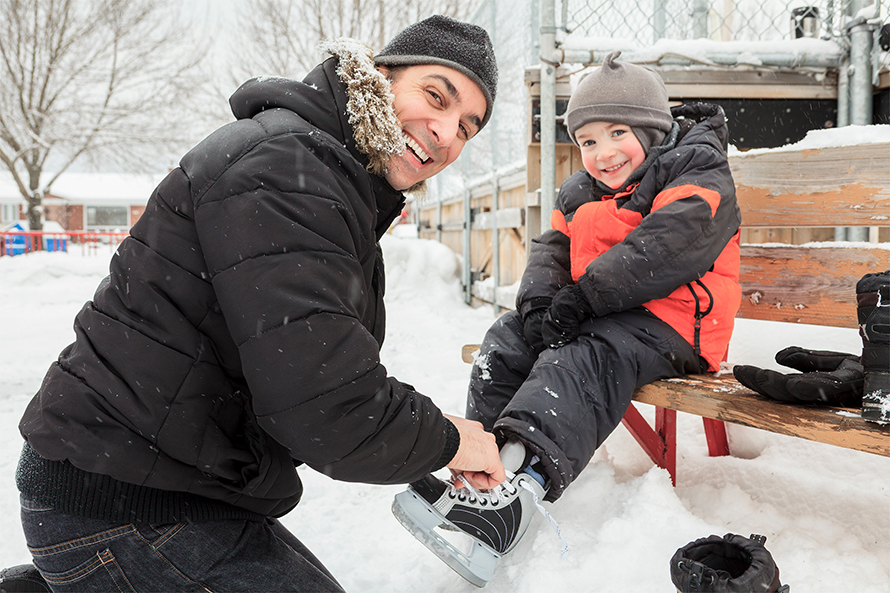 Man helping young boy tie skates. 